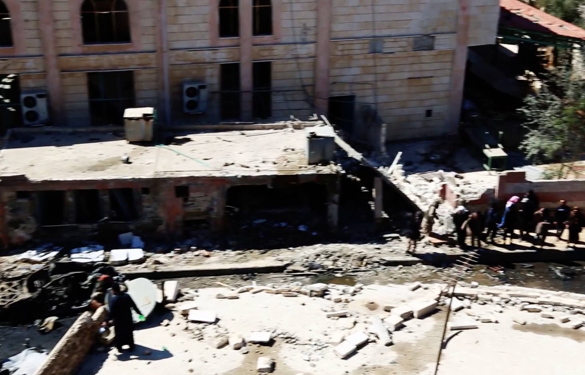 As locals look on at the destruction left by a US airstrike, the local mosque's distinctive windows can clearly be seen immdiately behind (Picture courtesy of Raqqa is Beng Slaughtered Silently)