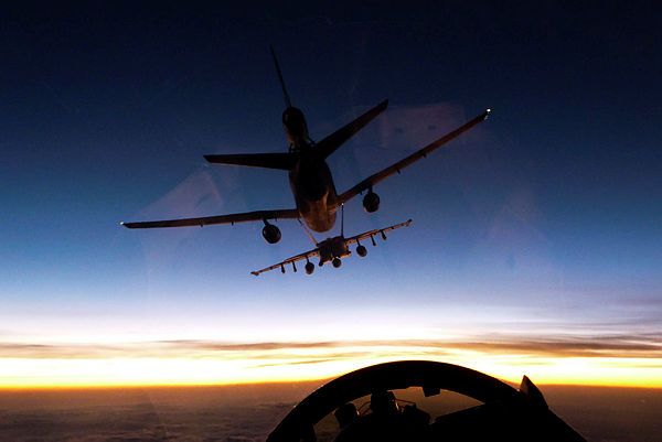 The wingman of a Royal Australian Air Force (RAAF) F/A-18F Super Hornet watches as his leader prepares to refuel from a United States Air Force KC-10A tanker aircraft mid-air as the sun sets over Iraq (Aus MoD)